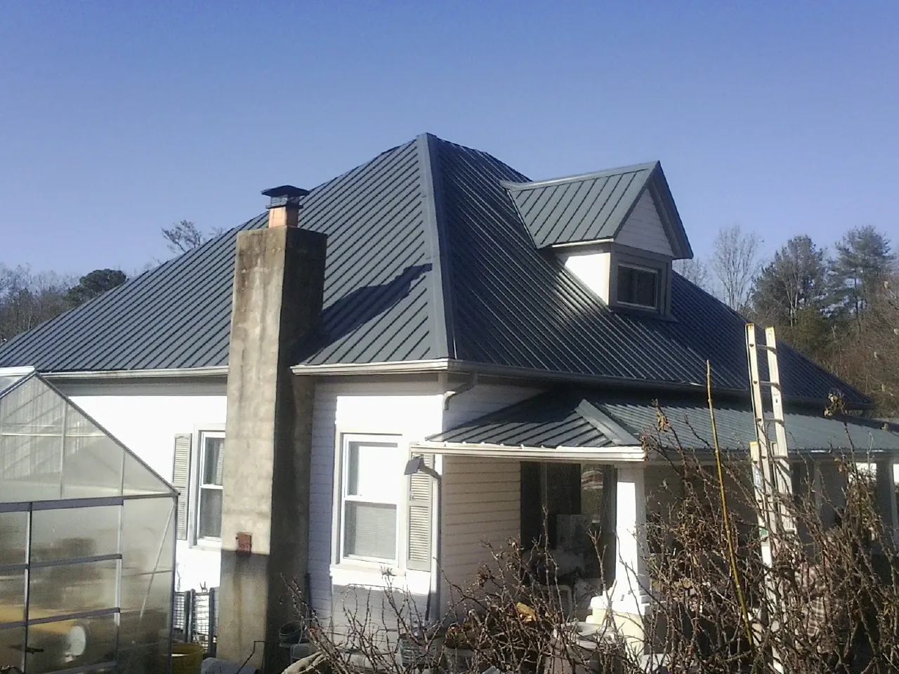 Dark blue standing seam metal roof on a white farmhouse with dormer — Slate & Tile Roof Repair by Roofing Brothers in Wallisville