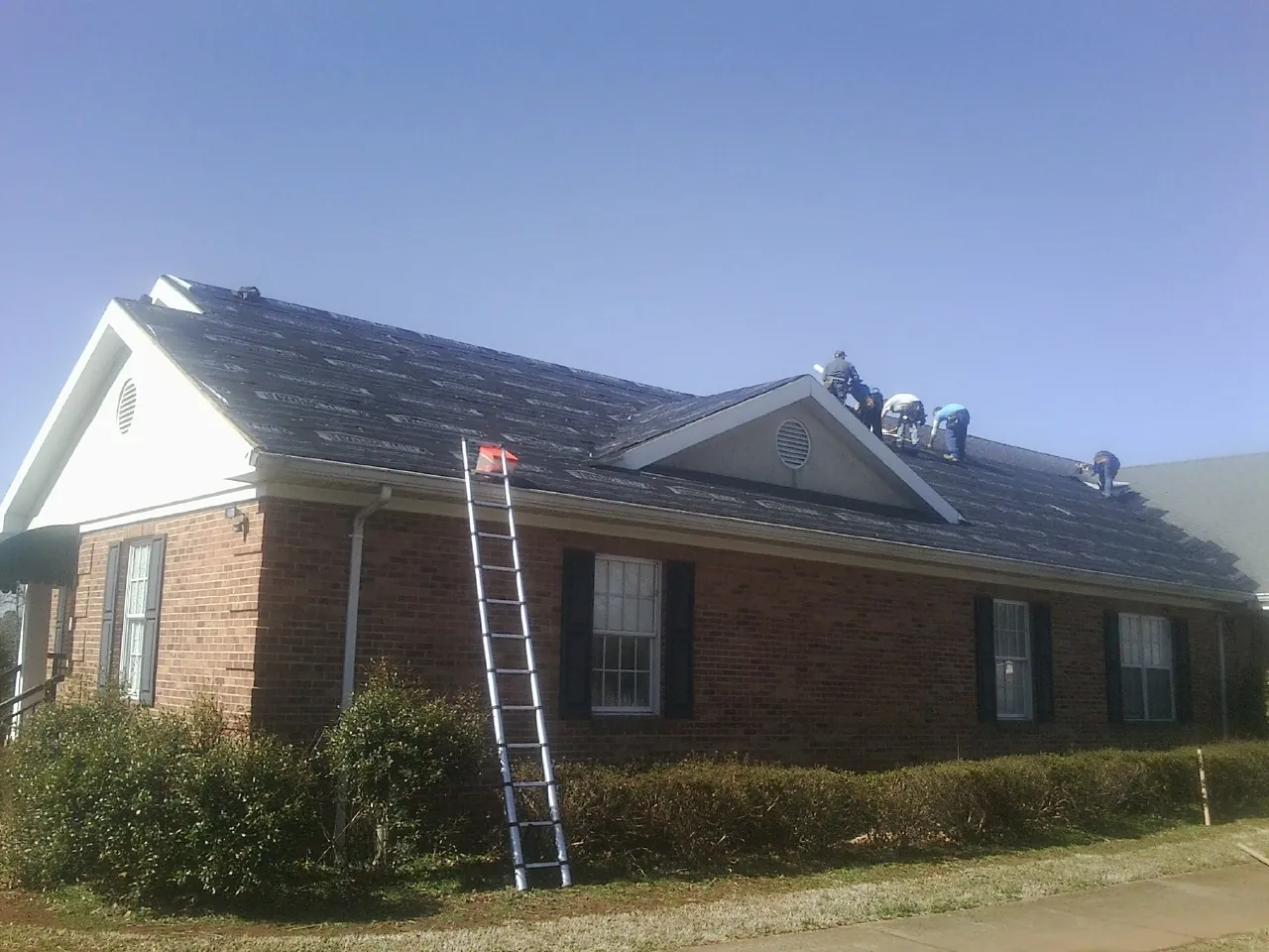 Crew tearing shingles off a brick ranch roof with a ladder set — Emergency Roof Repair work by our crew in Wallisville