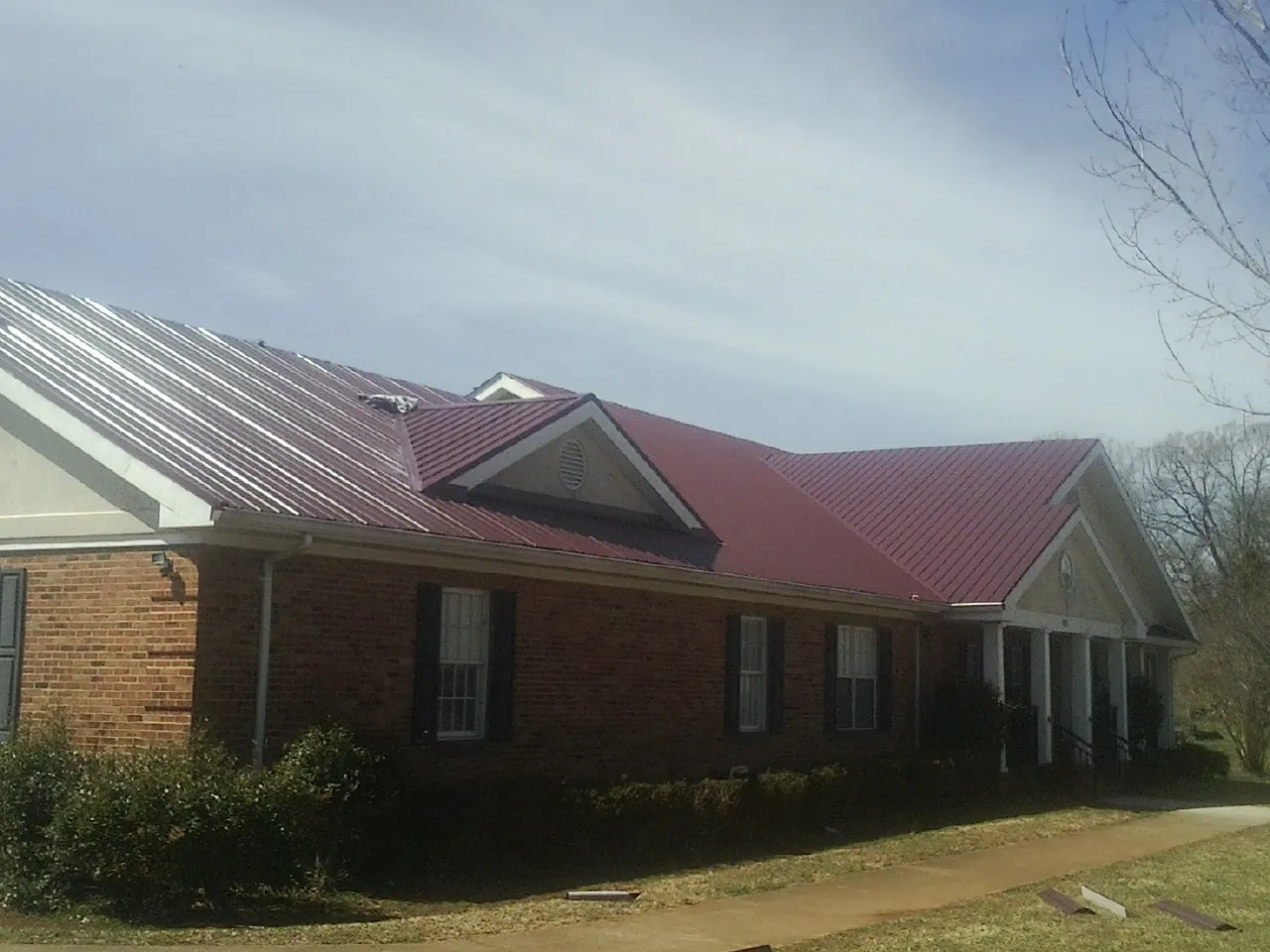 Red metal roof with gabled entries on a long brick building, from a Hail Damage Roof Repair job in Wallisville