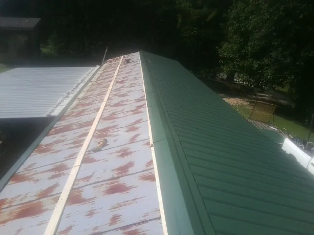 Old rusted panels beside newly installed green metal roofing — Wind Damage Roof Repair by Roofing Brothers in Wallisville