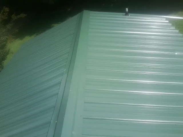 New green metal panels meeting at the ridge of a roof — Flat Roof Repair work by our crew in Wallisville