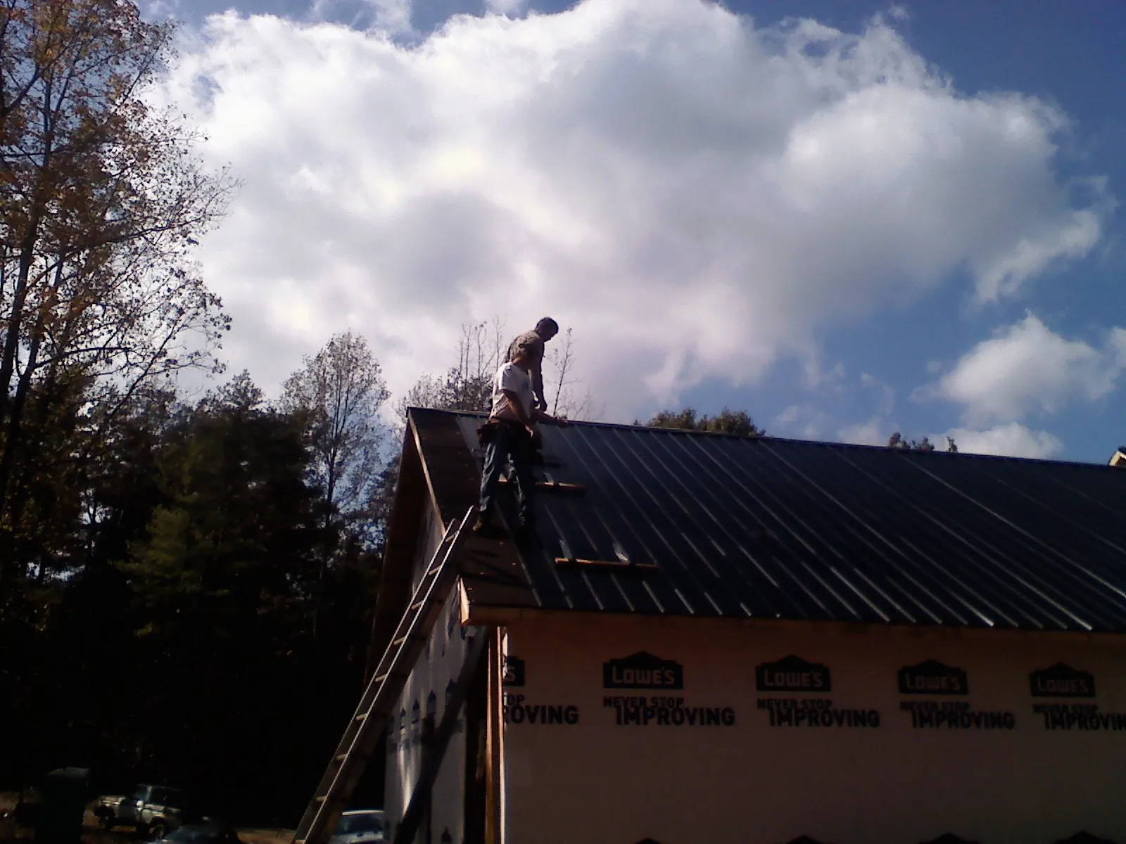 Roofer fastening dark metal panels high against a cloudy sky, from a Roof Inspection job in Wallisville