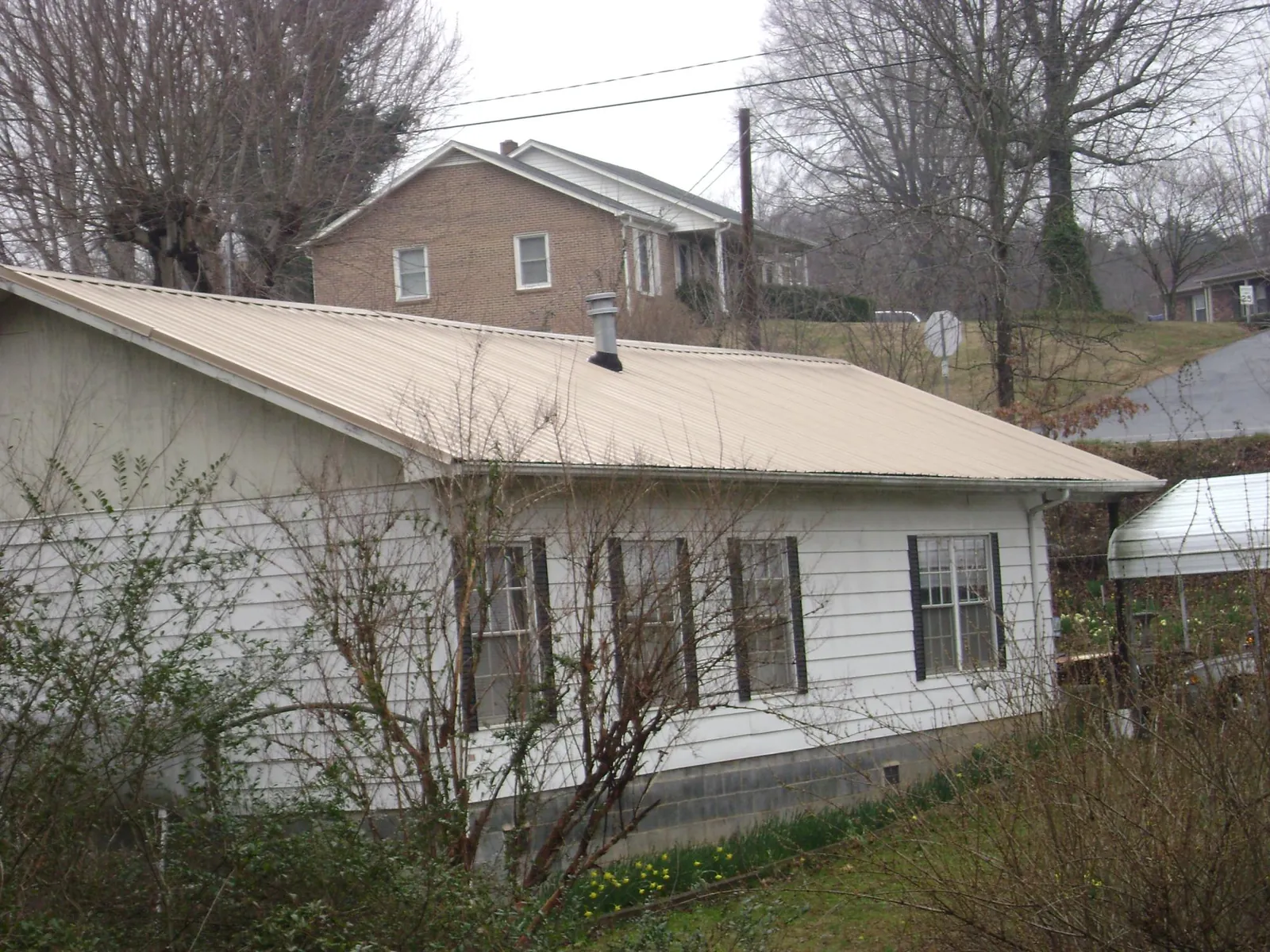Tan metal roof on a white sided house set into a hillside — Commercial Roofing by Roofing Brothers in Wallisville