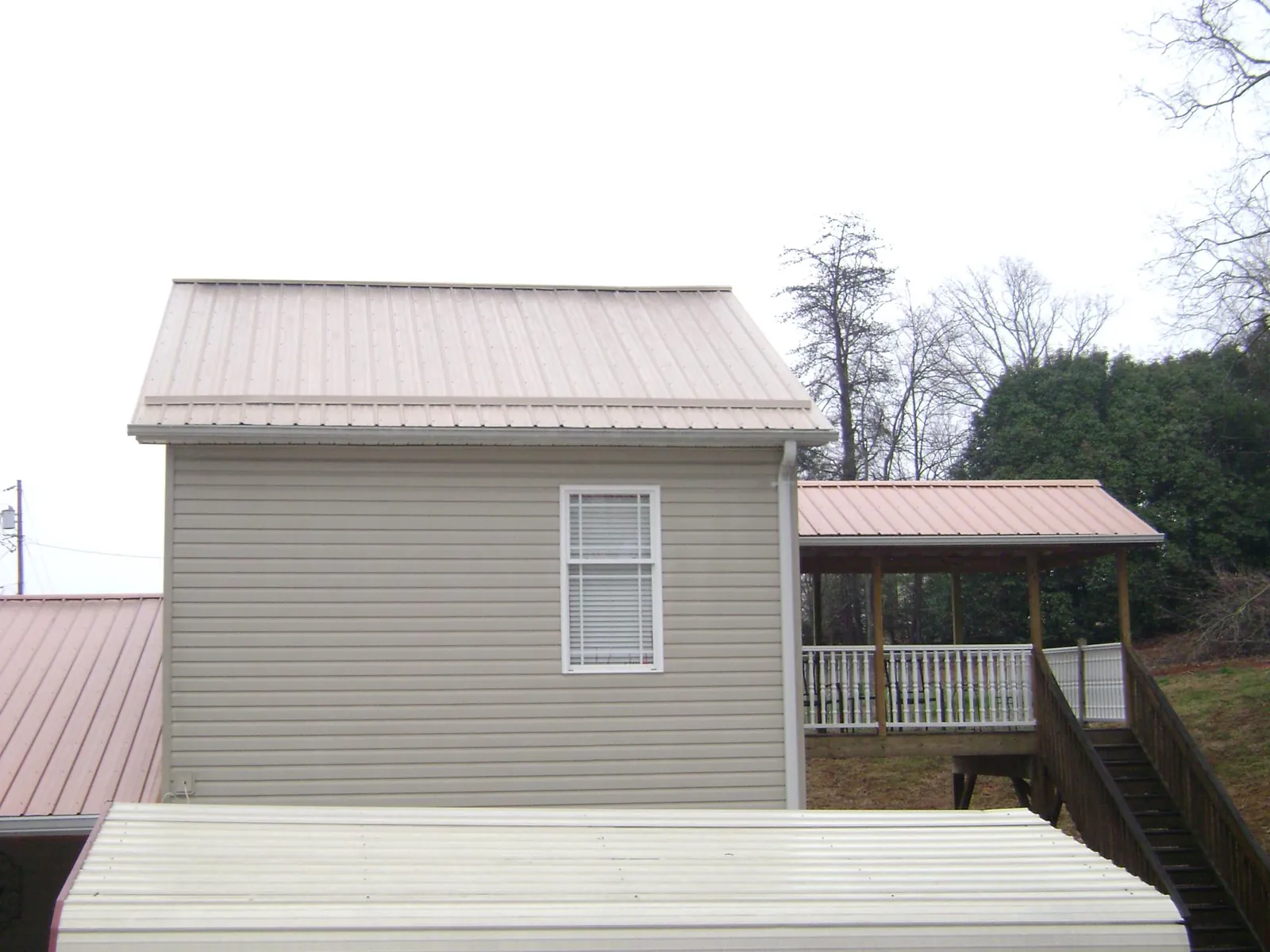 Tan metal roofs on a two story addition and attached porch, from a Roof Replacement job in Wallisville